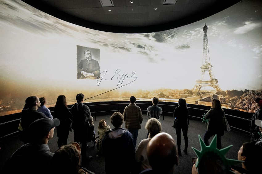 Crowd viewing a screen with Gustave Eiffel’s portrait and the Eiffel Tower.