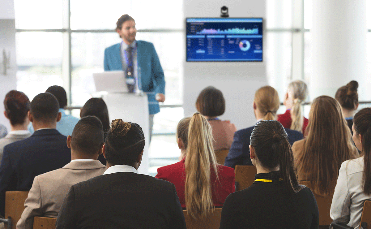An all-hands meting with he boss addressing his sitting employees, feature Q-SYS peripherals