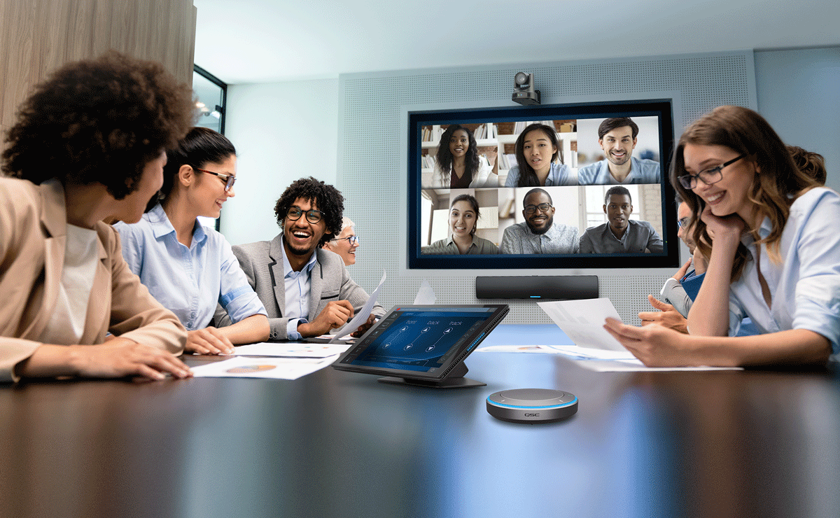 People sitting at a conference table with a Conference all on the display, featuring a variety of Q-SYS peripherals
