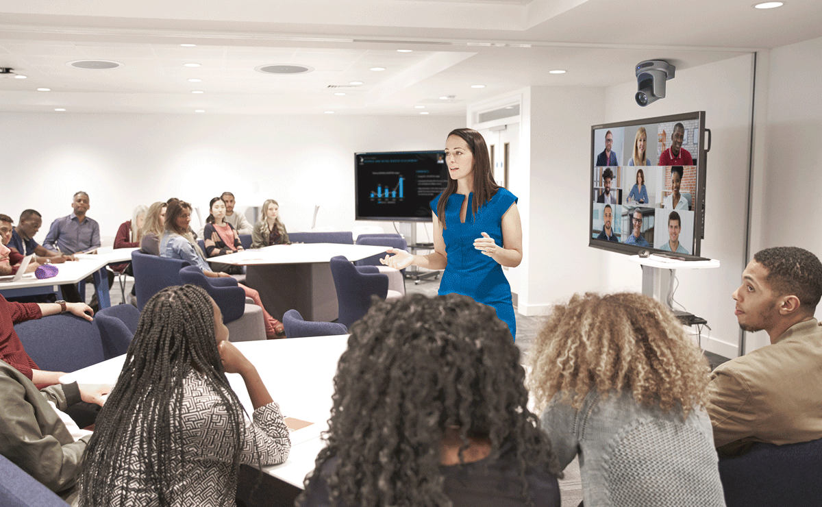 Woman speaking in the center of a classroom surrounded by students, featuring Q-SYS peripherals